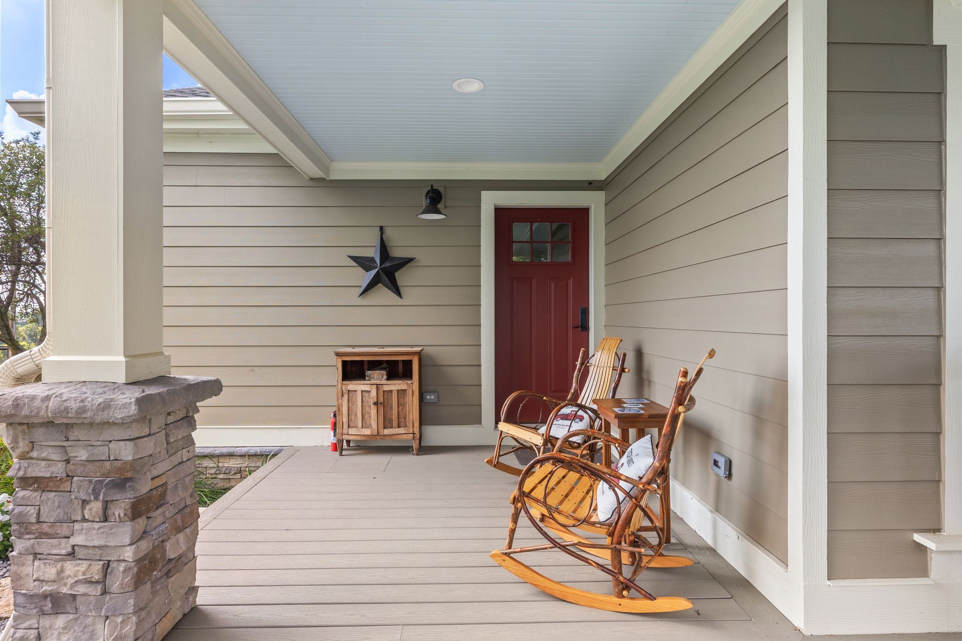 Covered front porch with rocking chairs, red door, and wooden cabinet.