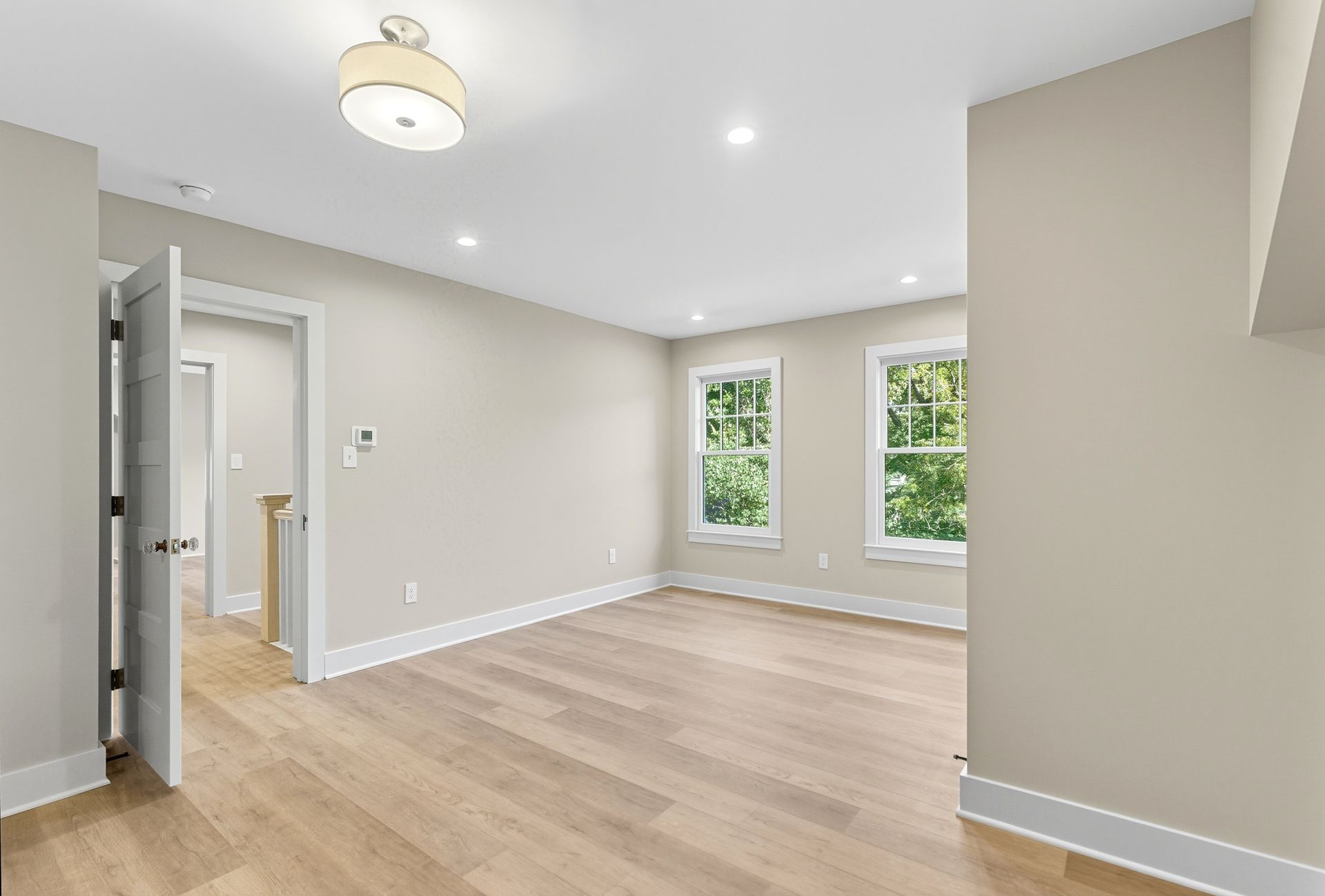 Empty room with light wood floor, beige walls, two windows, and an open doorway.