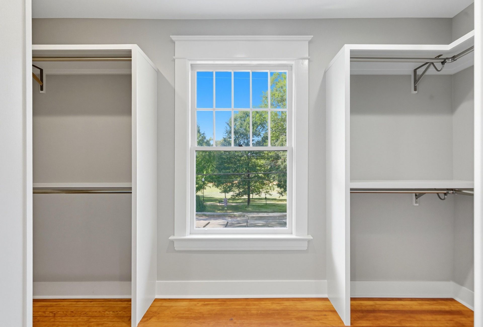 Empty closet with a window centered between the two openings, offering a view of a sunny landscape.