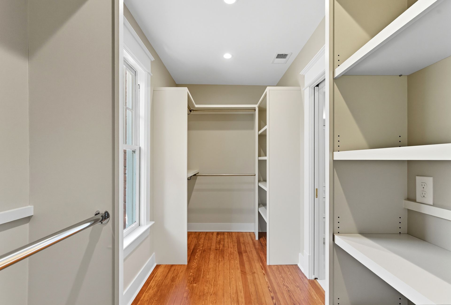 Walk-in closet with white shelves, hanging rod, and built-in storage on either side of a wooden floor.