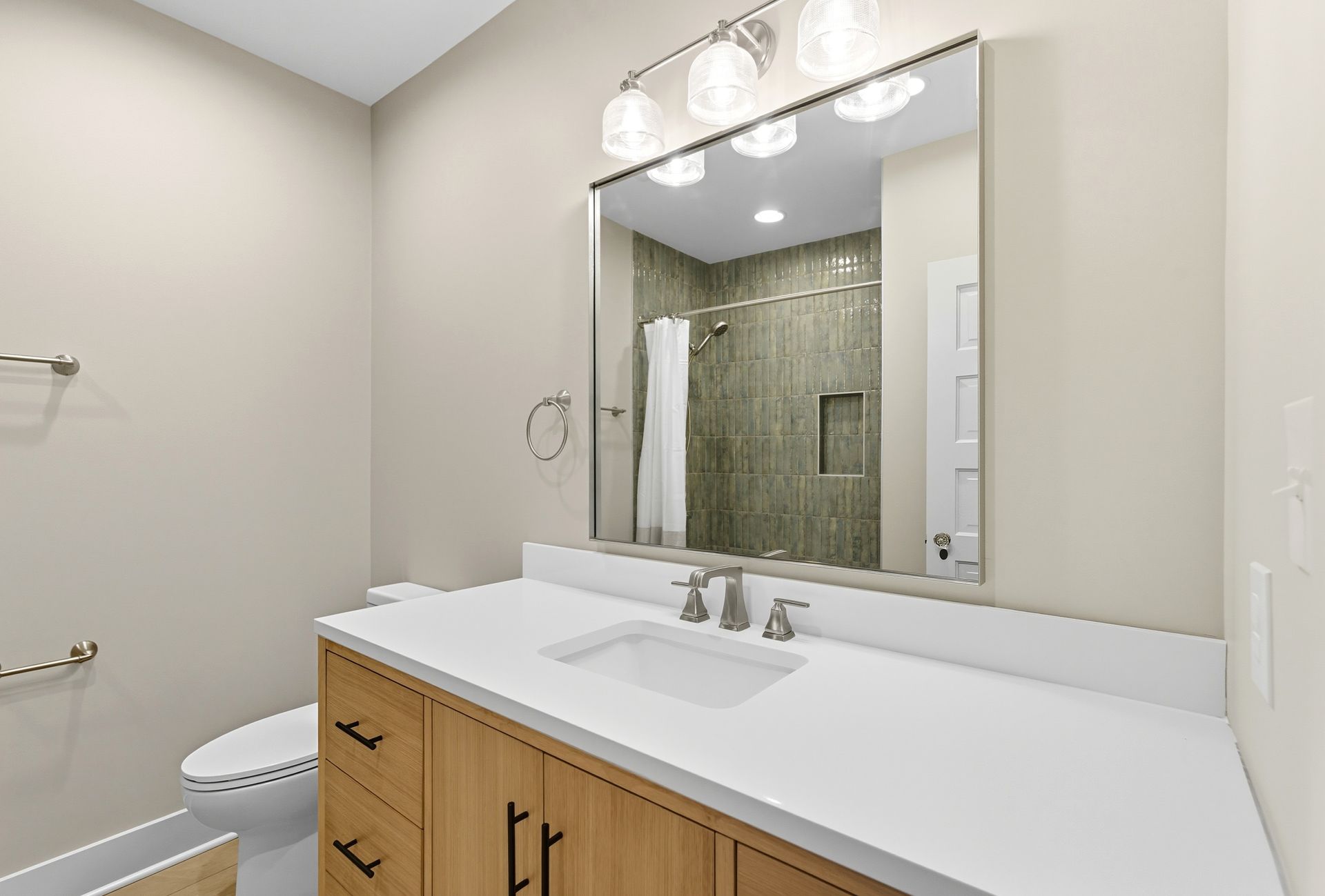 Bathroom with light wood vanity, white countertop, large mirror, and shower.