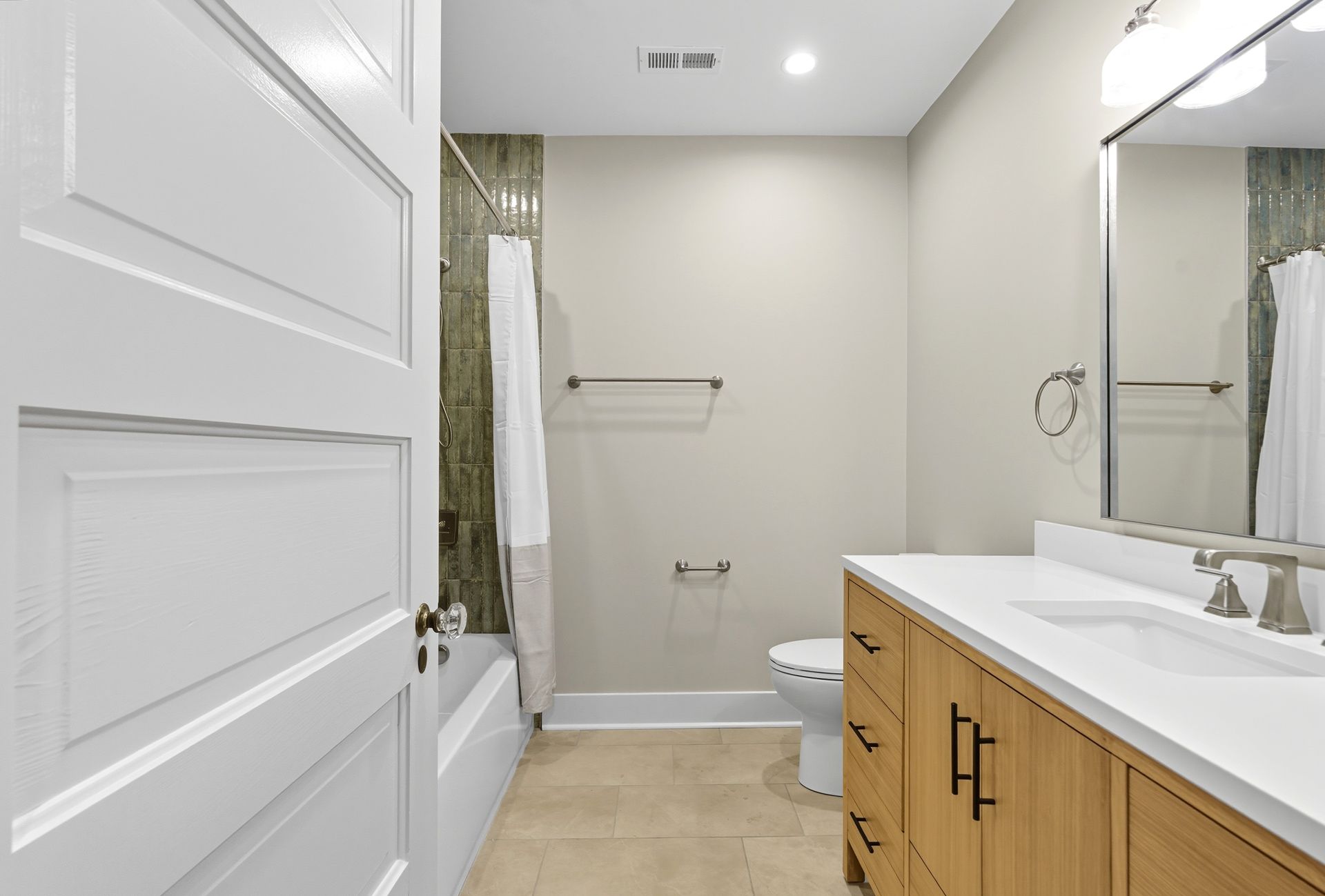 Bathroom with wood vanity, white countertop, toilet, bathtub with shower curtain, and open white door.