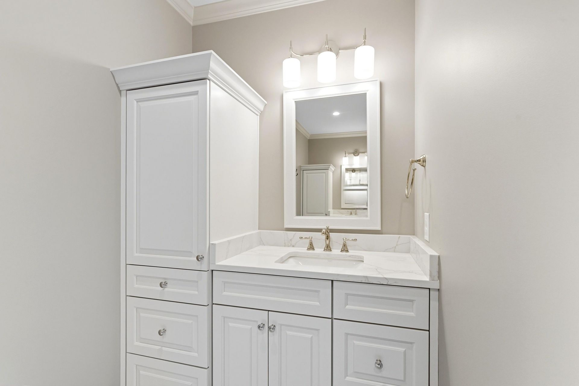 Bathroom with white vanity, tall storage cabinet, mirror, and three-light fixture.