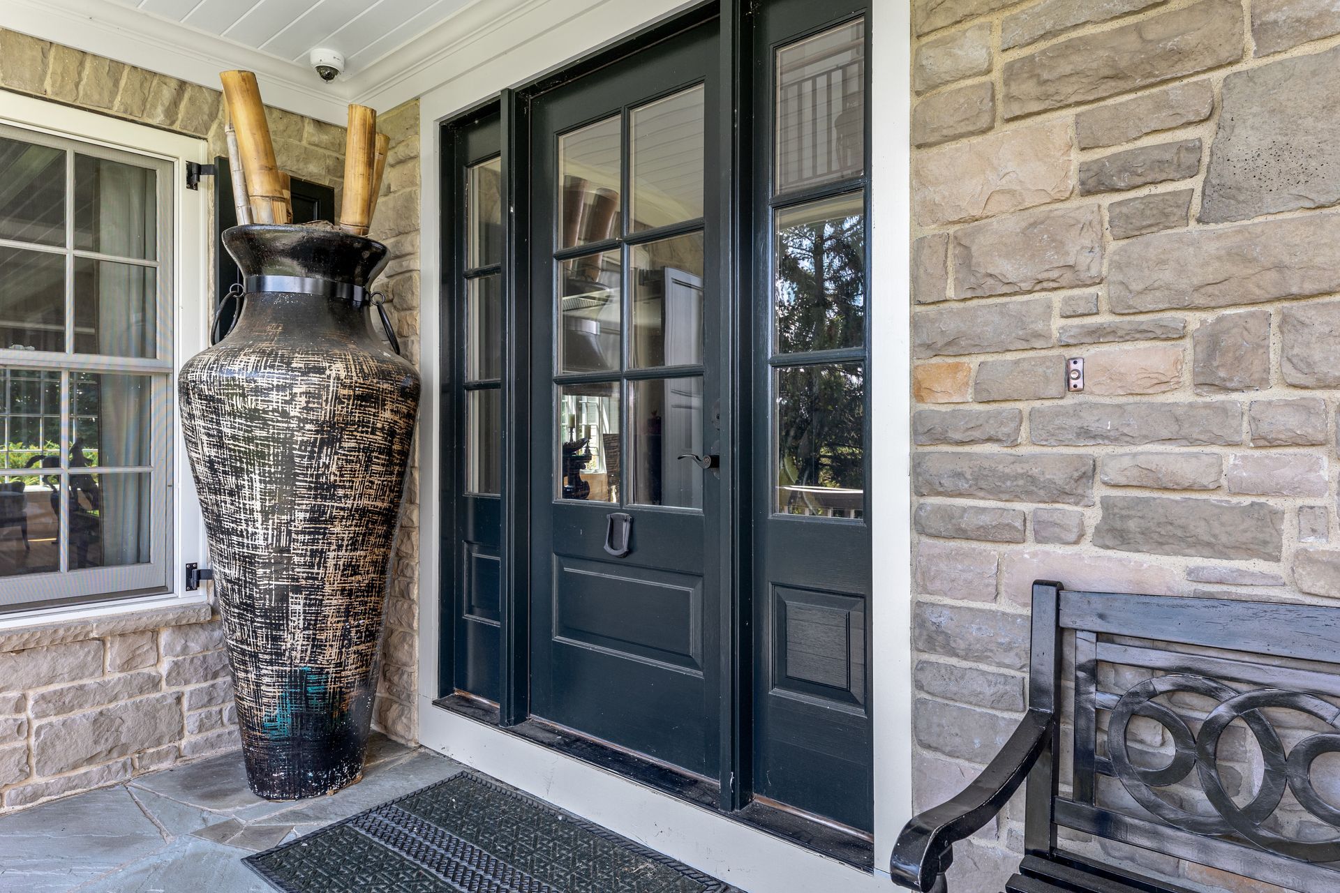 Dark blue front door, stone exterior, large decorative vase with bamboo, bench.