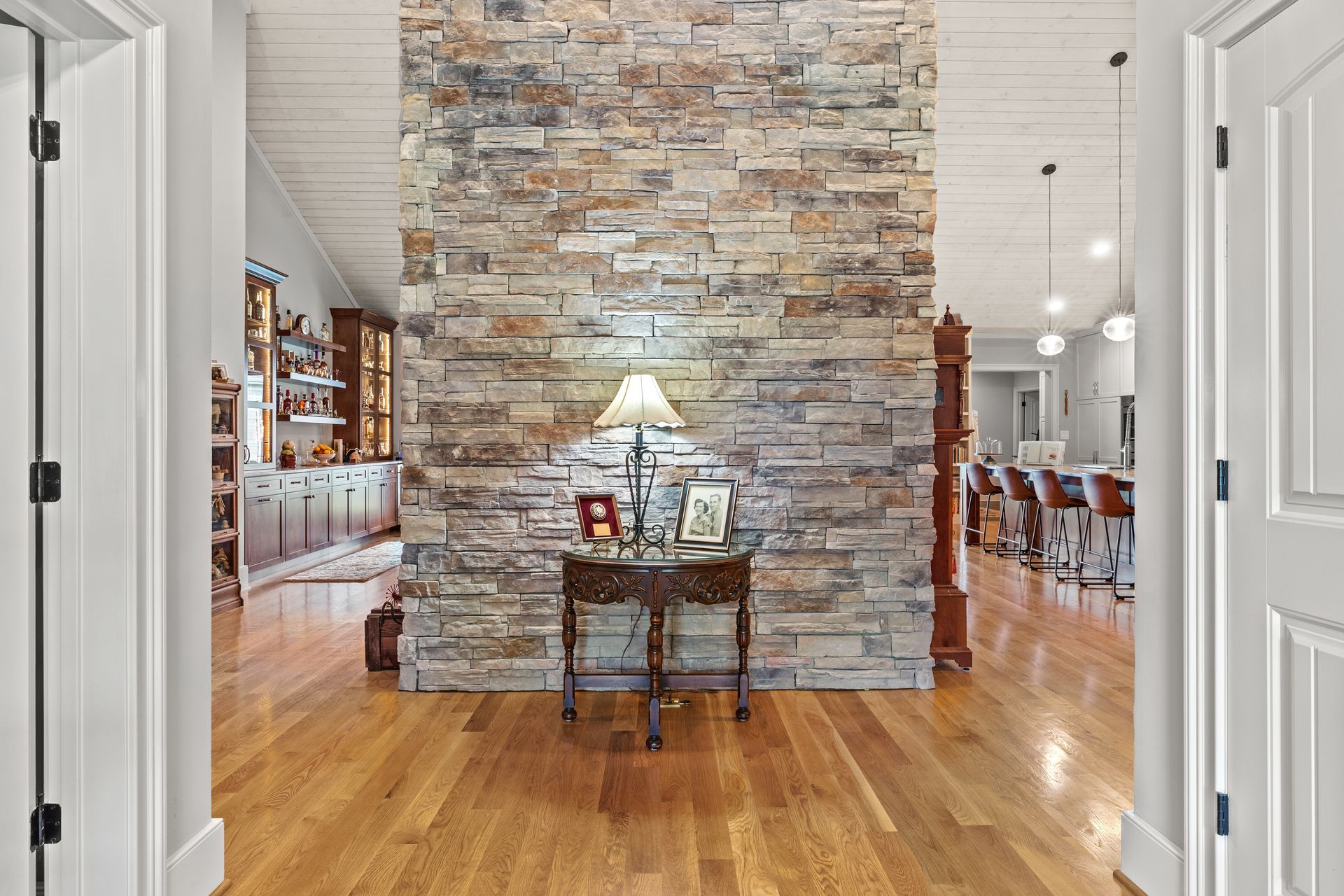 Hardwood floors lead to a stone wall, with a table and lamp. Doors frame the view.