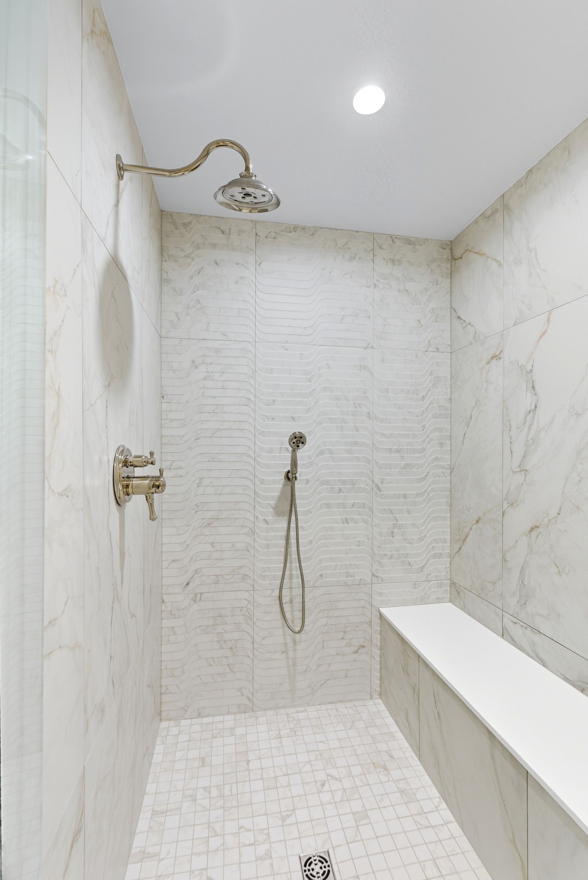 White tiled shower with a bench and shower head.