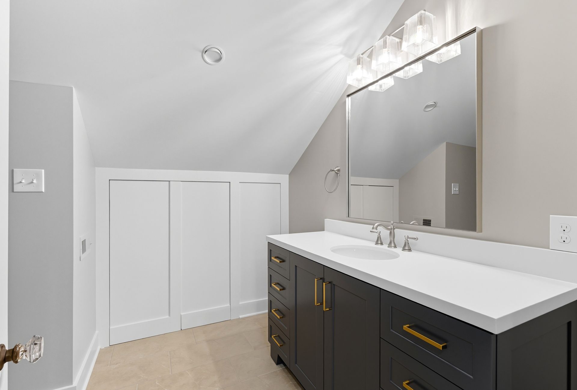 Bathroom with dark gray vanity, white countertop, and sloped ceiling.