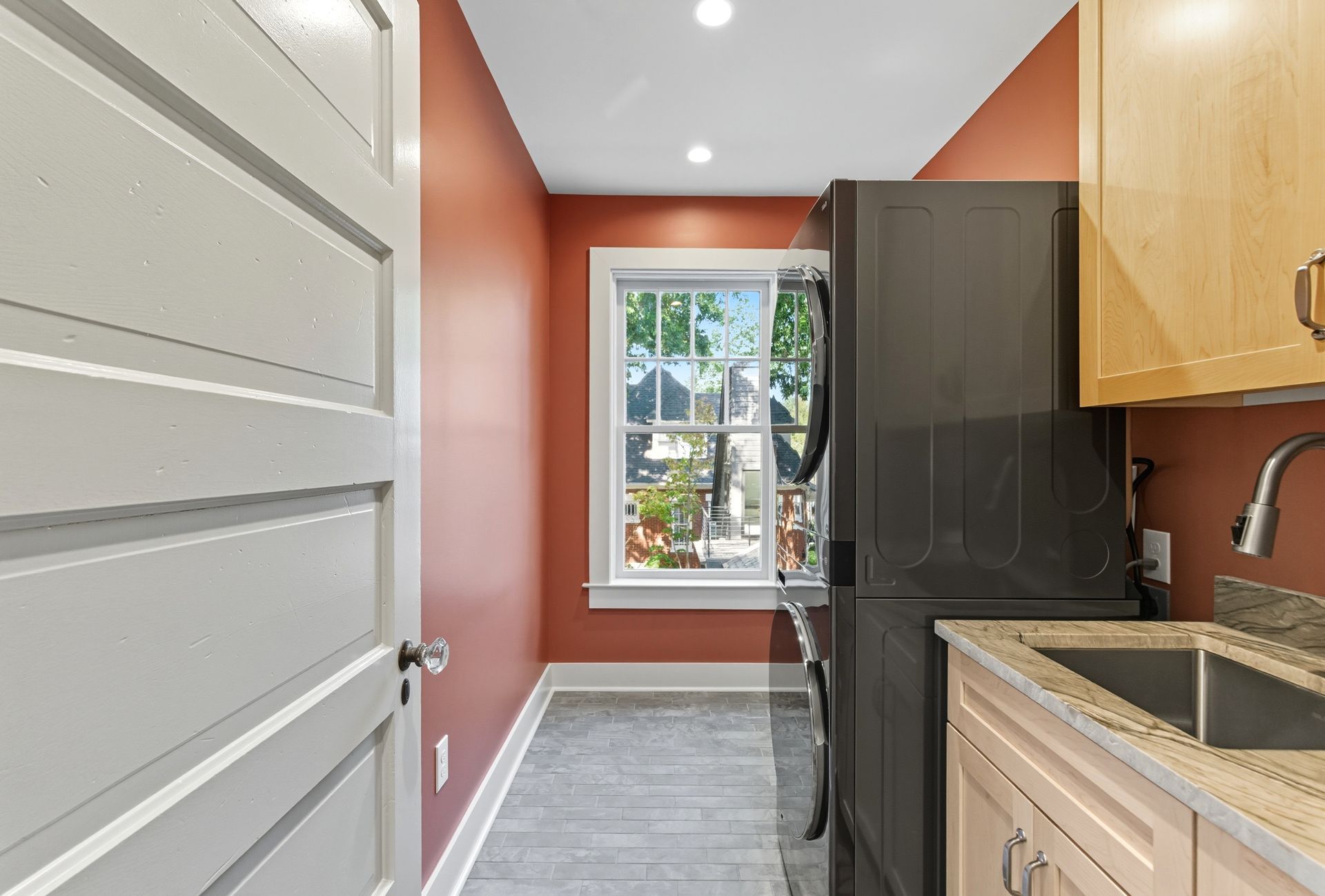 Laundry room with stacked washer and dryer, sink, red walls, and a window.