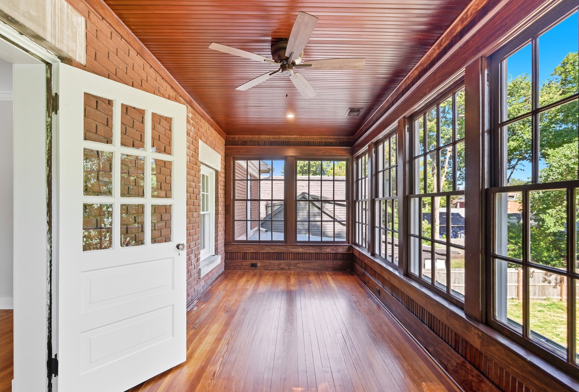 Sunroom with wood walls, ceiling, and floor. Large windows and a white door.