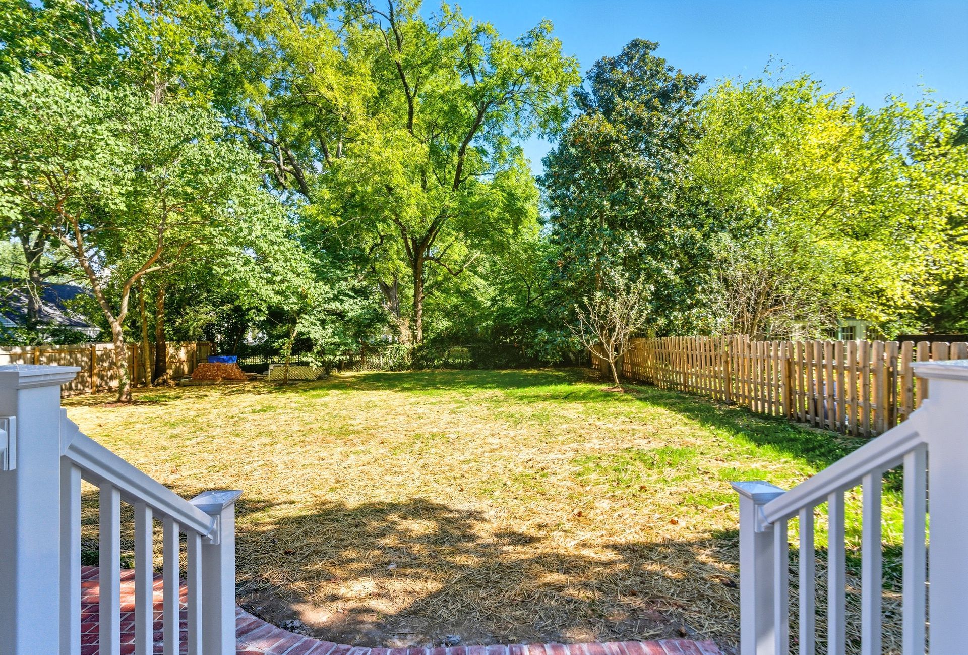 View from a porch into a backyard with a grassy area and trees surrounded by a wooden fence.