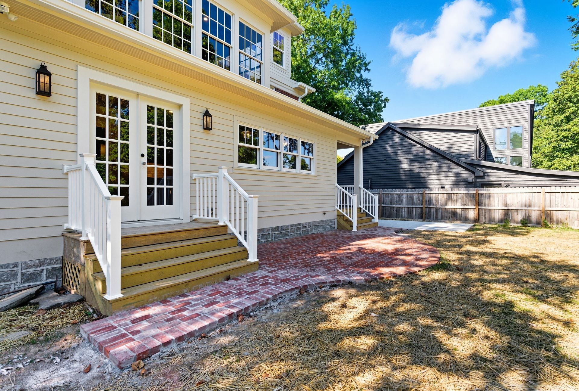 Beige house exterior with white French doors and brick pathway leading to yard.