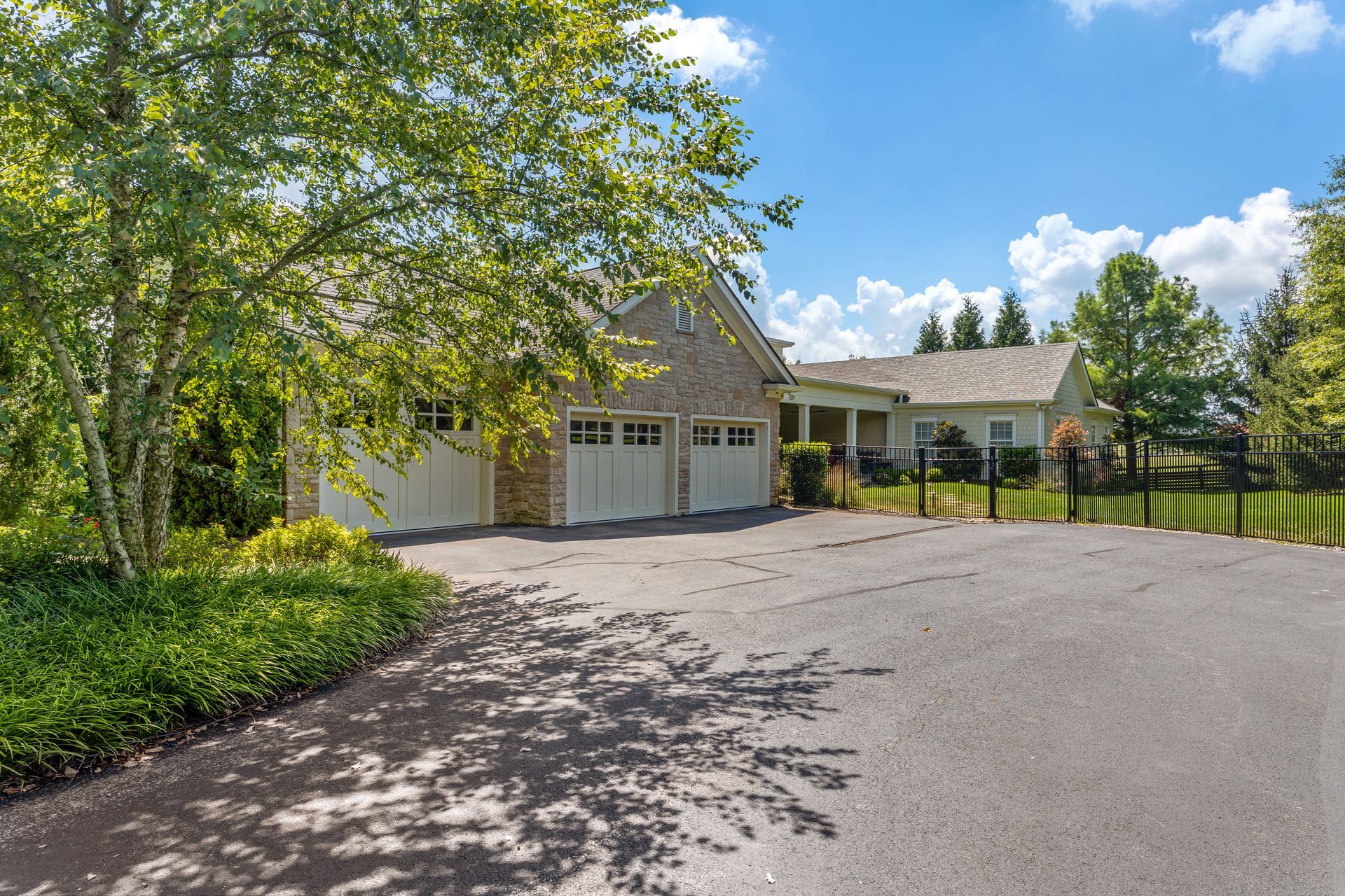House with attached garage, asphalt driveway, and lush greenery under a blue sky with fluffy clouds.