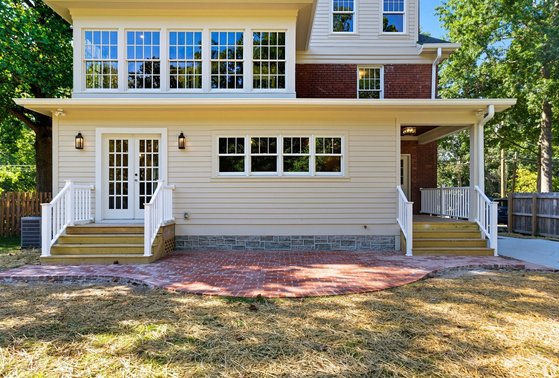 Back of beige house with patio, stairs, and windows. Brick patio, white railings.