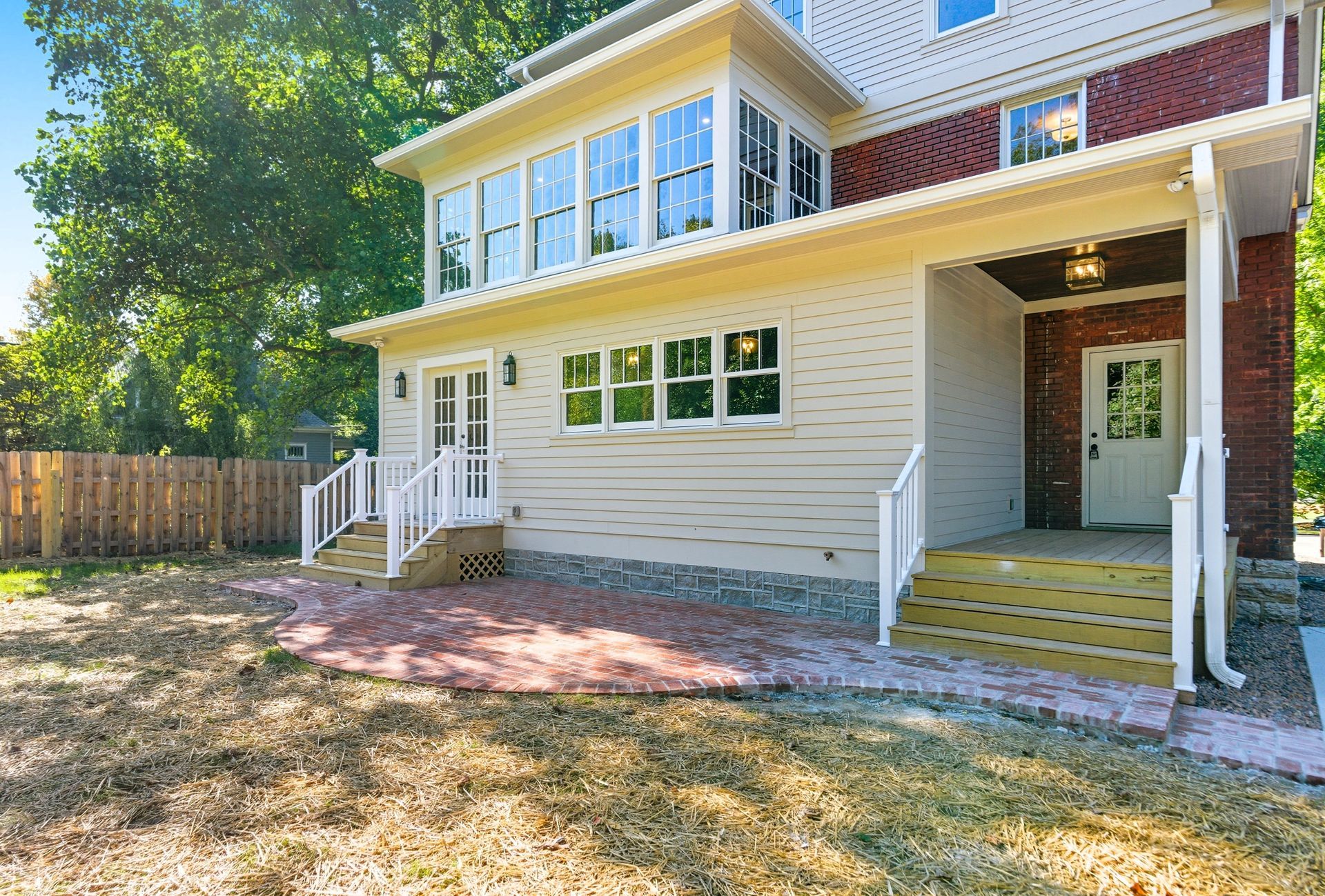 Two-story house with porch, windows, and brick accents. Yellow siding and a wooden deck.