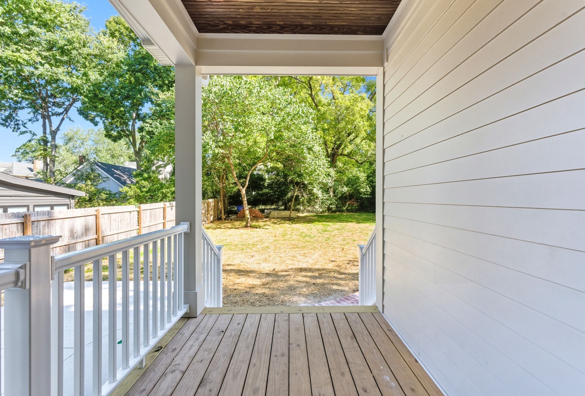 Porch view with white railing, wooden deck, and backyard with trees.