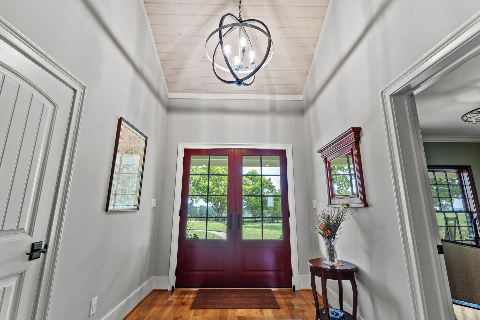 Entryway with red double doors, wood floor, and a decorative light fixture.