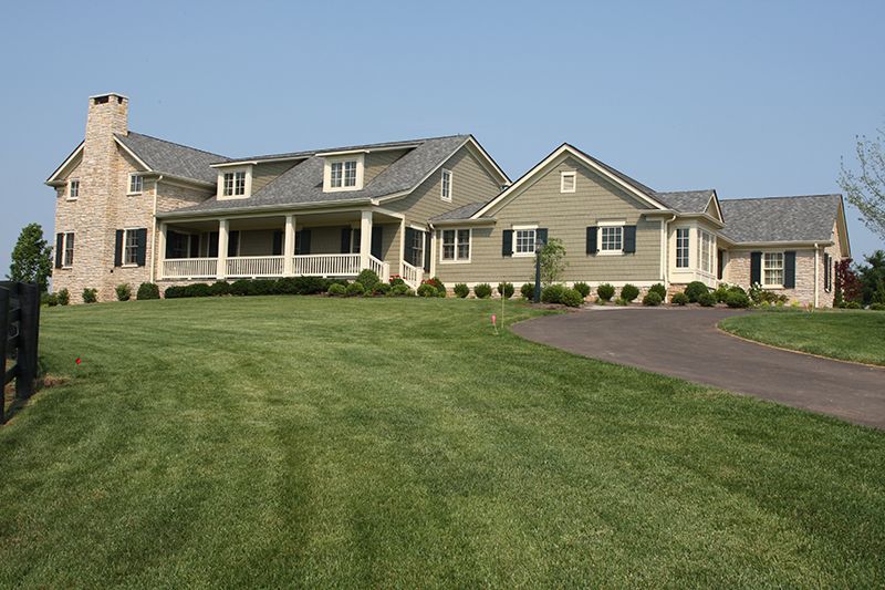 Large green house with a light green facade, brick chimney, and long winding driveway.