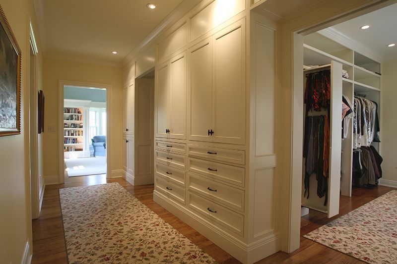 Hallway with white built-in wardrobes and drawers, leading to a closet. Wooden floor, floral rug.