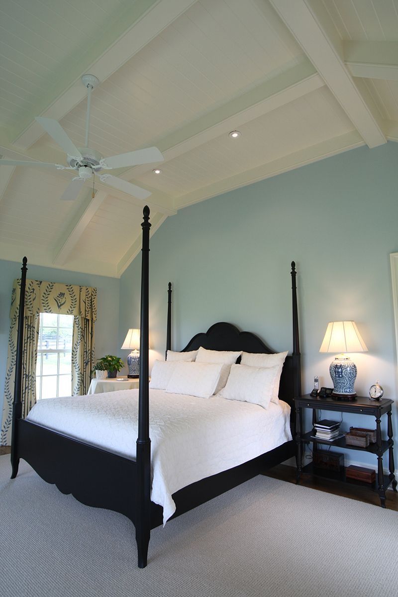 Bedroom with black four-poster bed, light blue walls, and white ceiling with beams; light gray carpet.