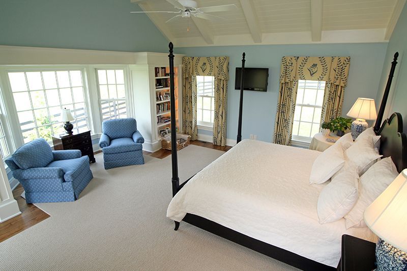 Bedroom with blue walls, a large bed, two blue armchairs, and windows with white trim.