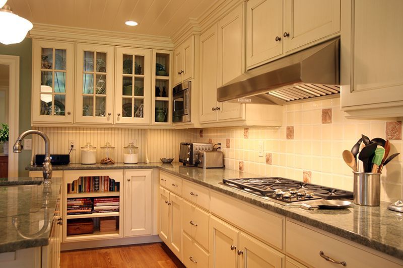 Cream-colored kitchen with granite counters, stainless steel hood, and glass-front cabinets.