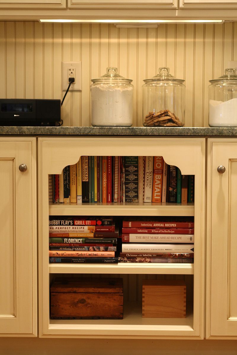 Cabinet with bookshelf in the middle, jars on the countertop. Books and boxes on the shelves.