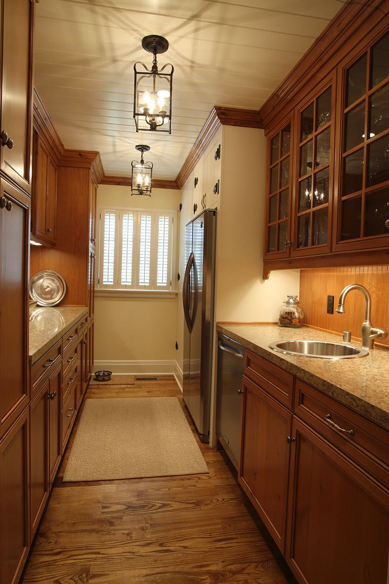 Narrow kitchen with wood cabinets, stainless steel appliances, and decorative lighting.