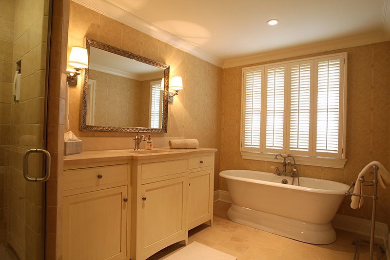 Bathroom with a white clawfoot tub, vanity, and window with shutter blinds. Beige walls and floor.