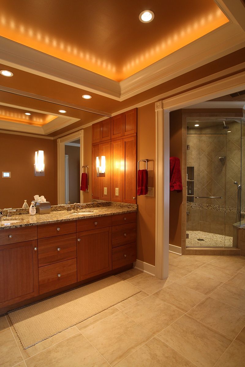 Bathroom with a vanity and a view of a shower. Warm colors with wood cabinets.
