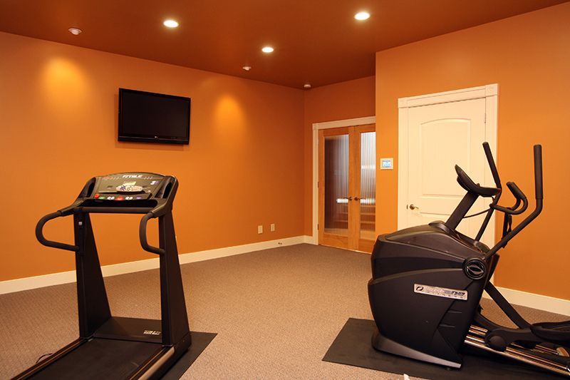 Home gym with orange walls, treadmill, elliptical, TV, and double doors.