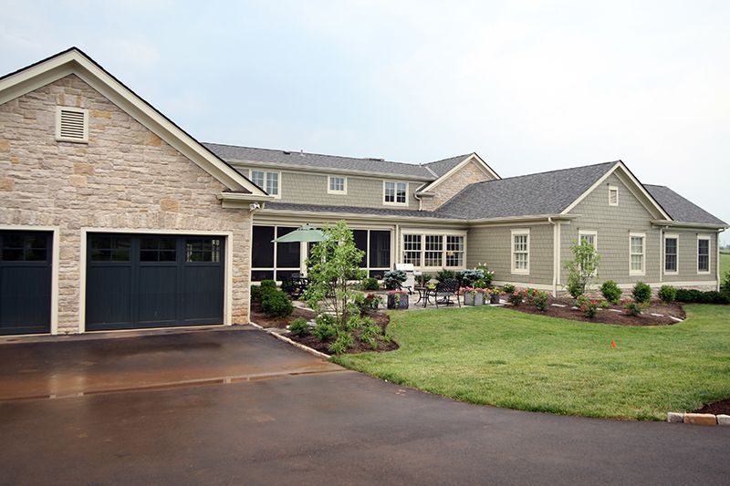House with stone garage, green siding, a screened porch, and a manicured lawn.