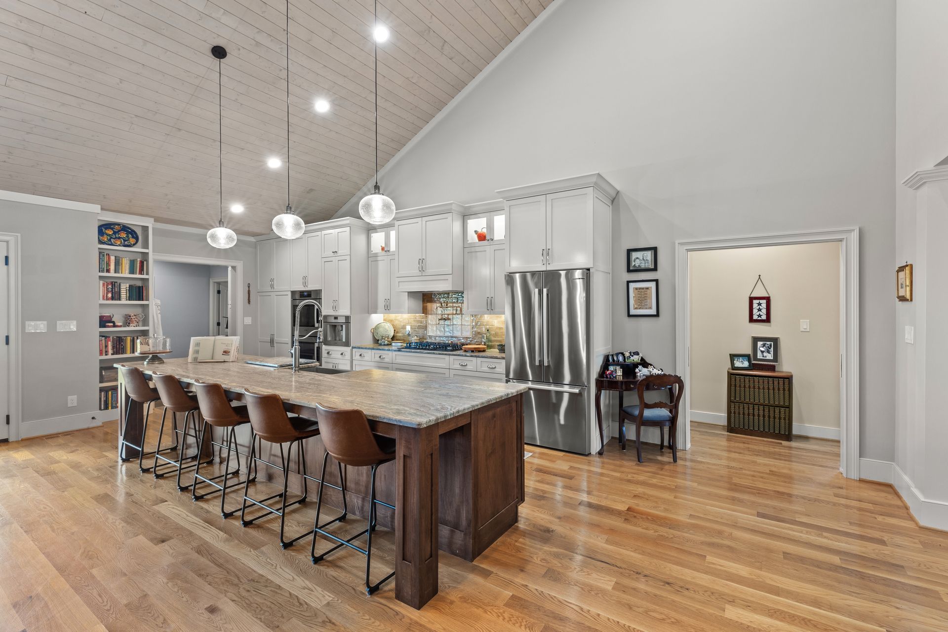 Spacious kitchen with a large island, hardwood floors, and high ceiling with pendant lights.