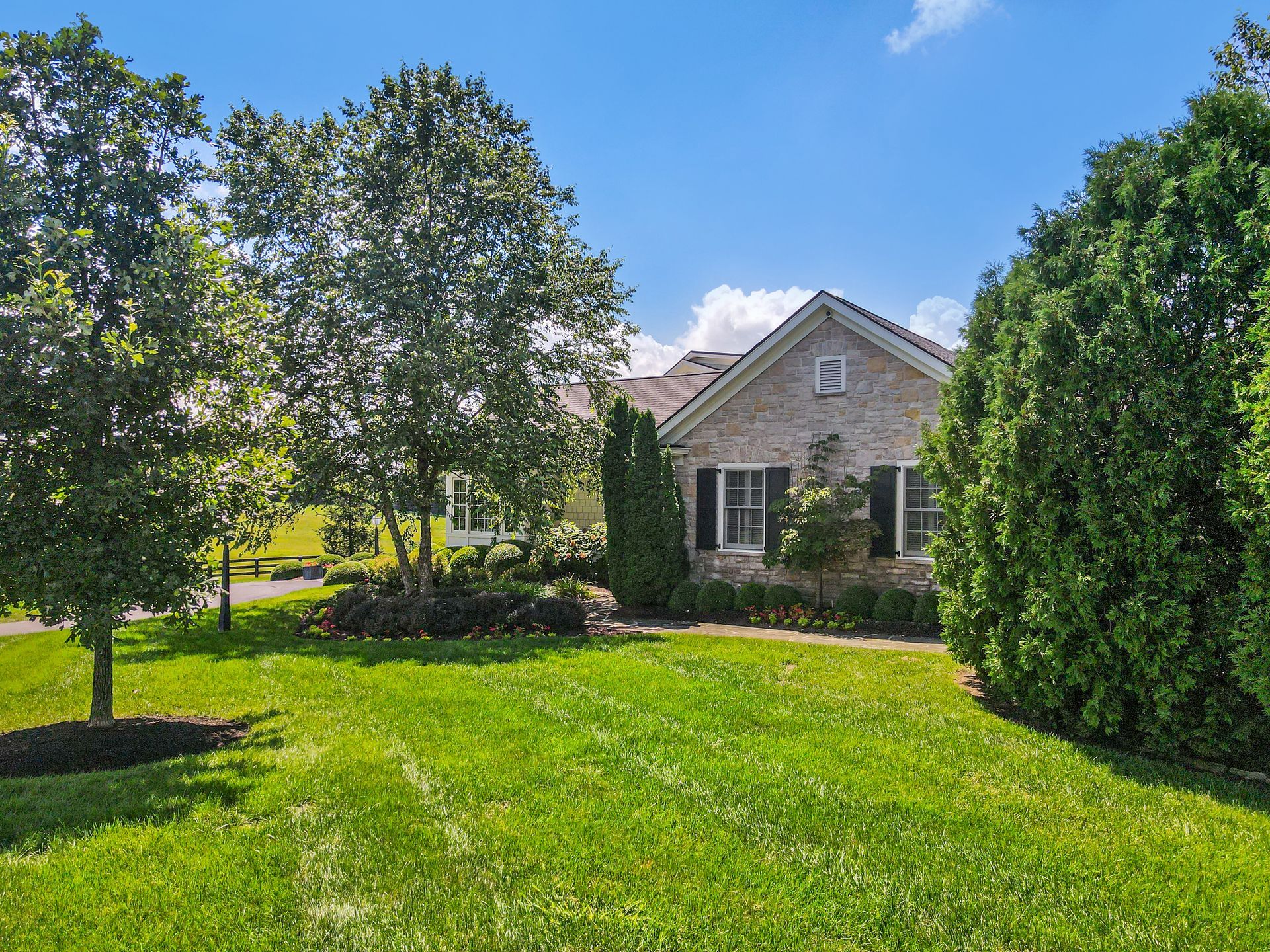 A single-story brick house with black shutters, surrounded by green grass and trees on a sunny day.