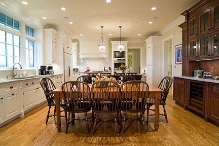 Spacious kitchen with a long wooden dining table and chairs. White cabinets and hardwood floor.