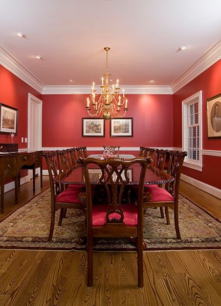 Red dining room with a long wooden table, chairs with red cushions, and a gold chandelier.
