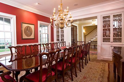 Formal dining room with red walls, long table, and ornate chandelier.