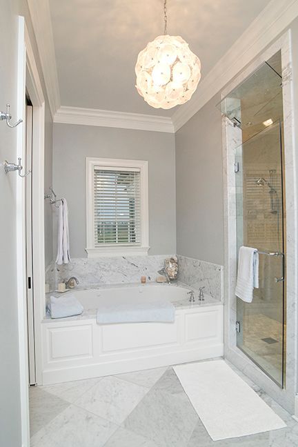 Elegant bathroom with a white tub, glass shower, marble accents, and a decorative light fixture.