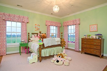 Child's bedroom with green walls, pink curtains, a wooden bed, a dresser, and a pink rug.