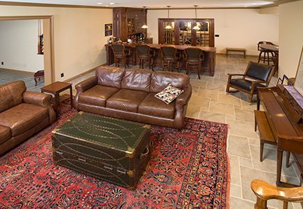 A finished basement with a brown leather sofa, bar, rug, and piano.