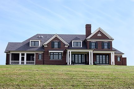 Large brick house with black shutters, white columns, and a green lawn.
