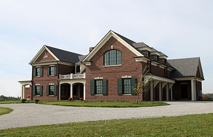 Brick house with black roof, green shutters, and a gravel driveway on a grassy lawn.