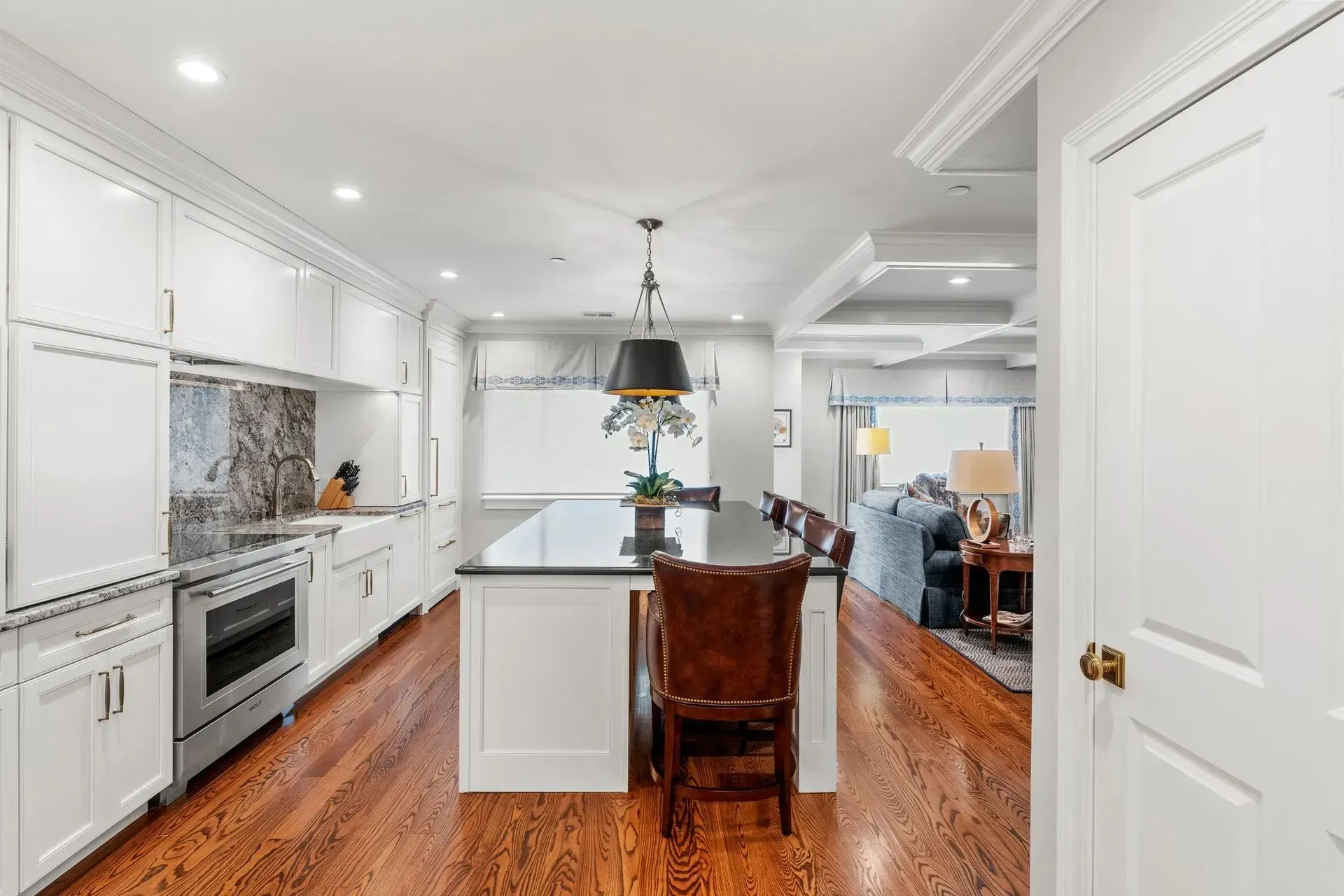 White kitchen with an island, hardwood floors, and a view of the living room.