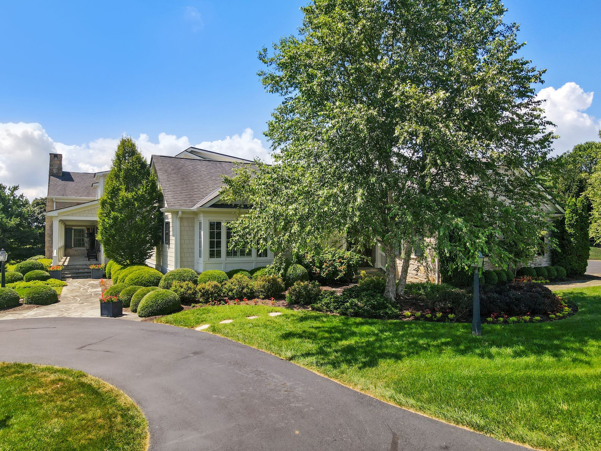 White house with green lawn and driveway, under a blue sky.