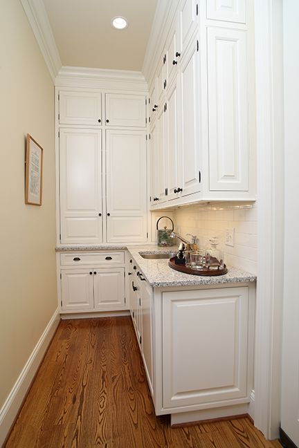 Narrow, white kitchen with wooden floor and granite countertops. Cabinets line walls, creating a corner sink area.