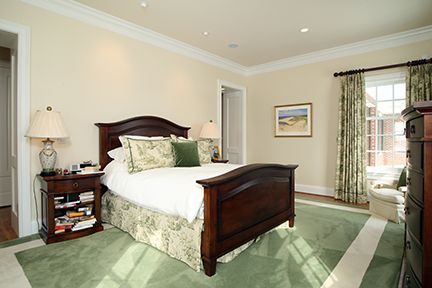 Bedroom with a dark wooden bed, green rug, and patterned curtains.
