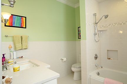 Bathroom with white fixtures, green wall, art, and shower.