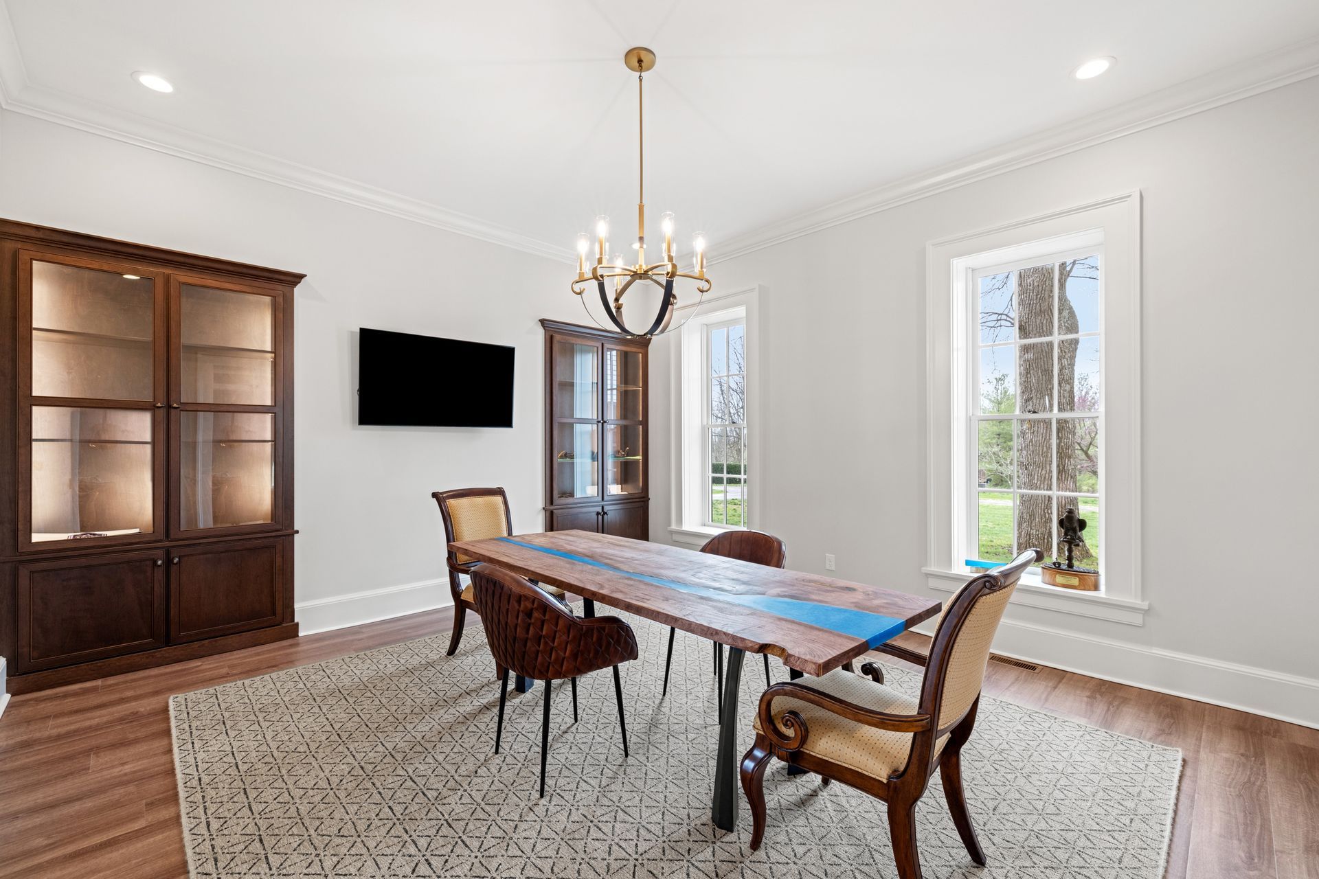 Dining room with wooden table, chairs, rug, chandelier, and cabinetry.