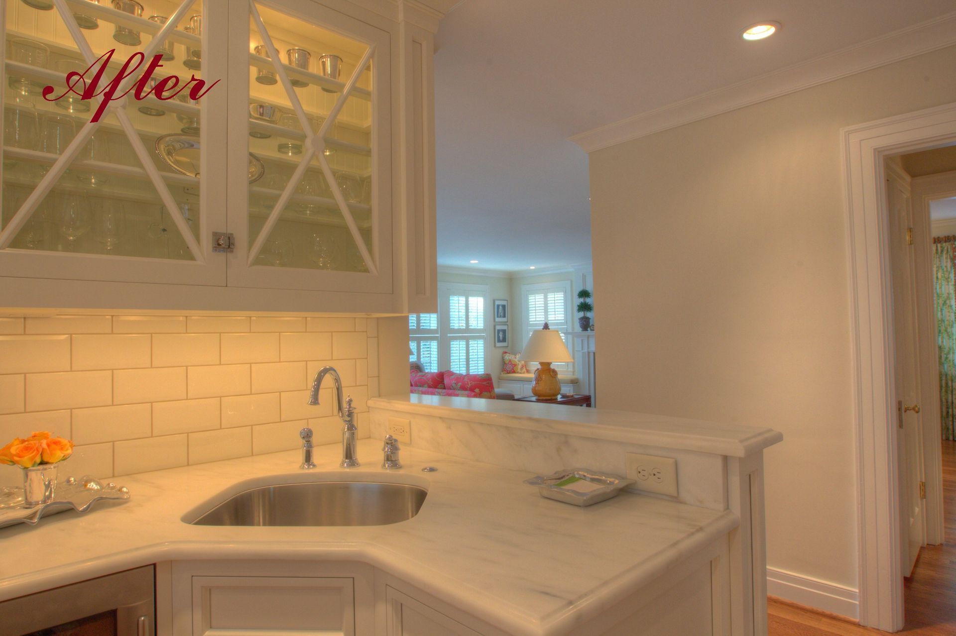 A renovated kitchen corner with a sink, glass-front cabinets, and a marble countertop, seen from an angle.