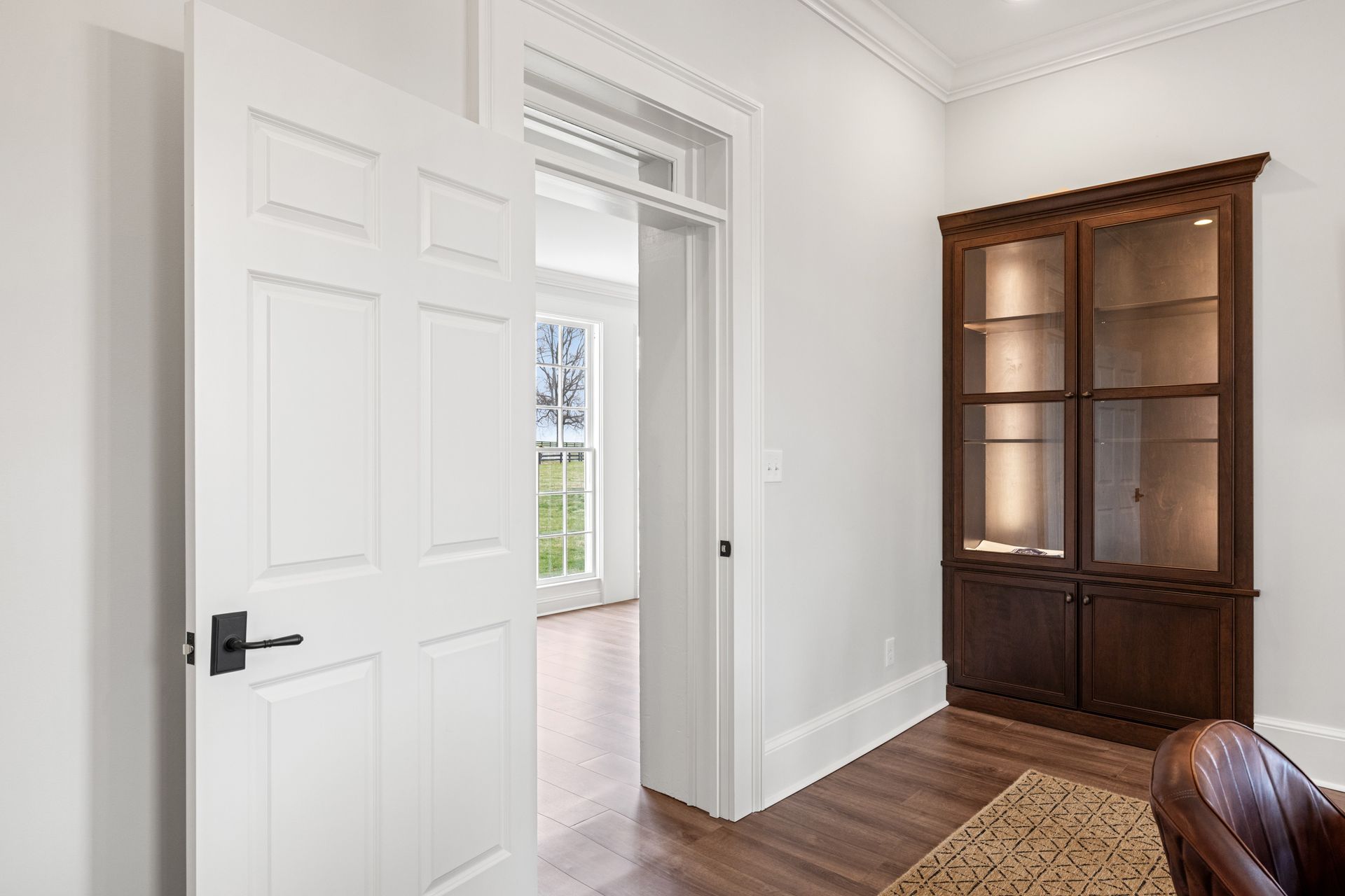 White door partially open to an empty room with a window. A dark cabinet is on the right.