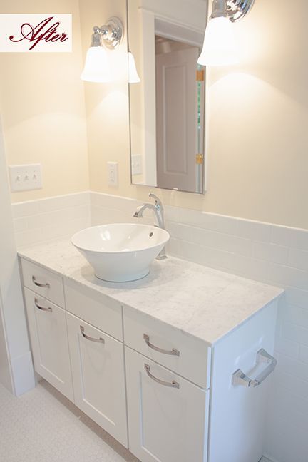 White bathroom vanity with a vessel sink, lights, and a mirror; the walls are cream-colored.